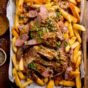 A tray of golden chips topped with sliced steak, creamy Peppercorn Sauce, and chopped parsley.
