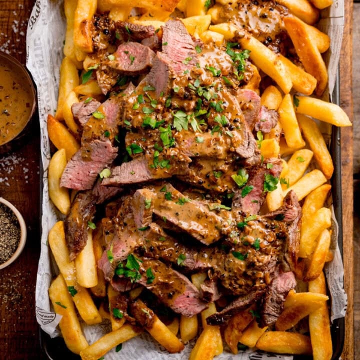 Steaky Chips with Peppercorn Sauce Square FS A tray of golden chips topped with sliced steak, creamy Peppercorn Sauce, and chopped parsley.