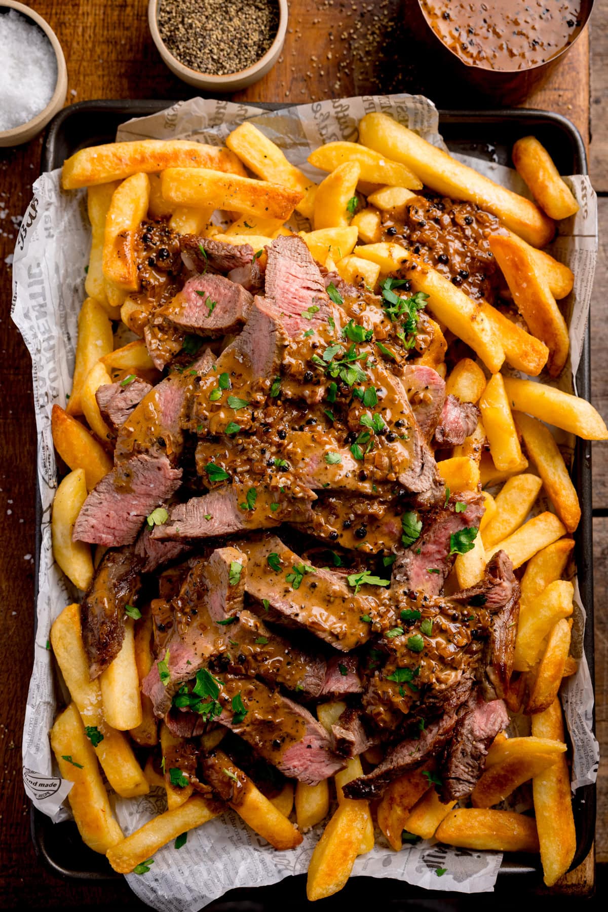 A tray of Steaky Chips—chips topped with sliced steak, peppercorn sauce, and chopped parsley, surrounded by little pots of salt, pepper, and extra peppercorn sauce.