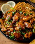 A plate of Lemon Pepper Chicken with sesame seeds and sliced spring onions, served with noodles and lemon slices.