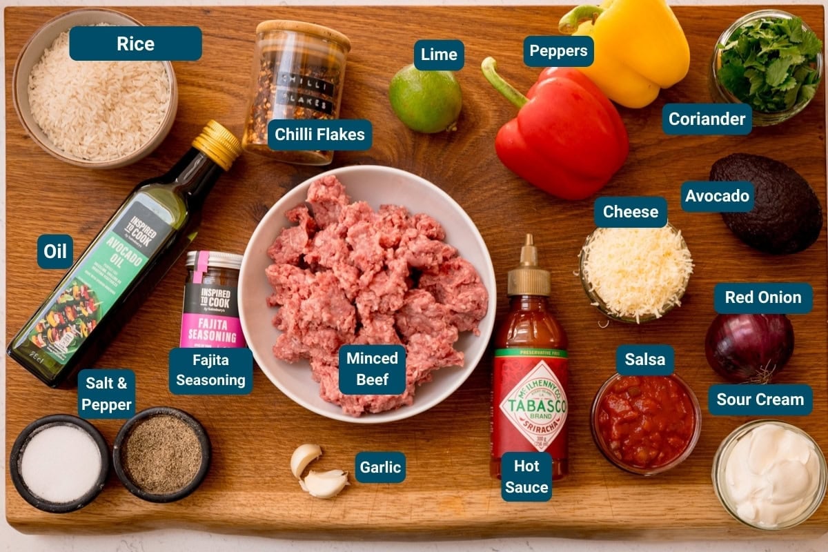 A wooden board displays labelled ingredients for making beef fajita bowls, including minced beef, rice, vegetables, spices, oil, cheese, salsa, avocado, soured cream and hot sauce.