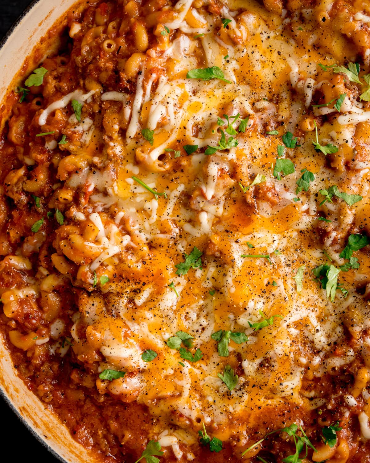 Close-up of one pot minced beef mac n cheese topped with melted cheese, garnished with chopped parsley and cracked black pepper.