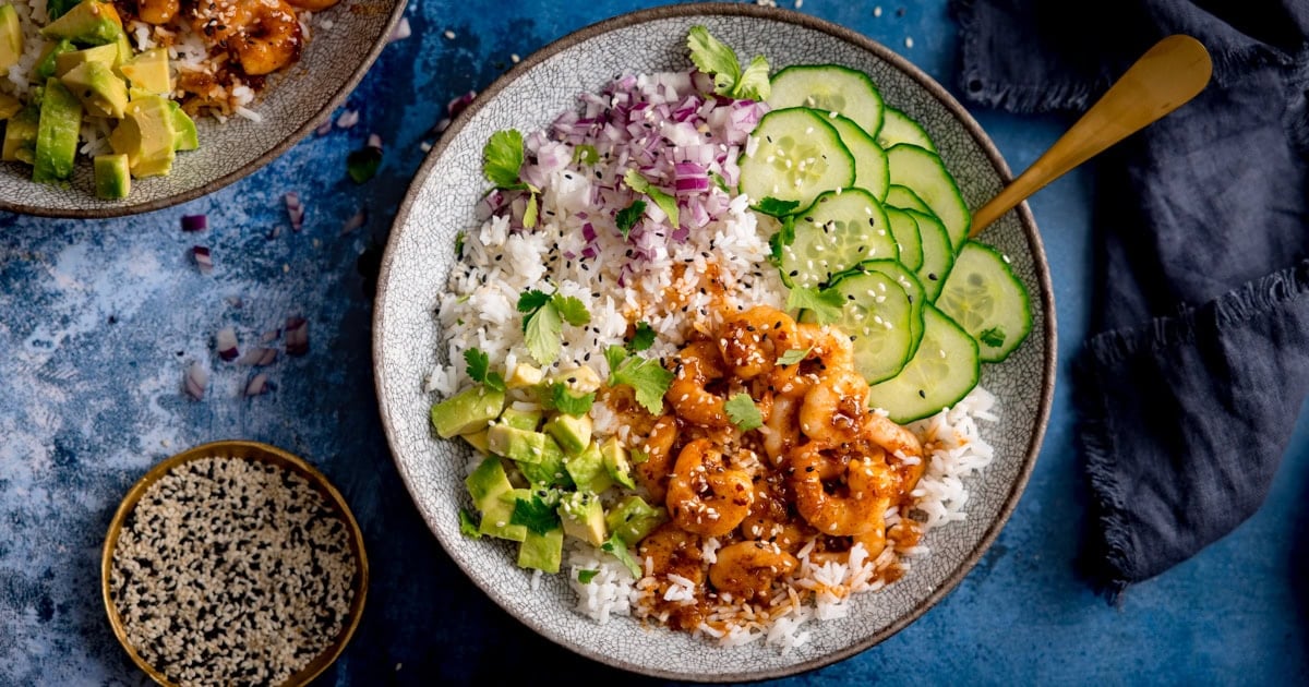 a bowl of white rice topped with honey prawns, diced avocado, sliced cucumber and diced red onion.