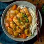 A bowl of Chicken Katsu Curry with rice, breaded chicken fillets, sliced carrots and potatoes, shredded cabbage, and chopped spring onions, served with chopsticks.