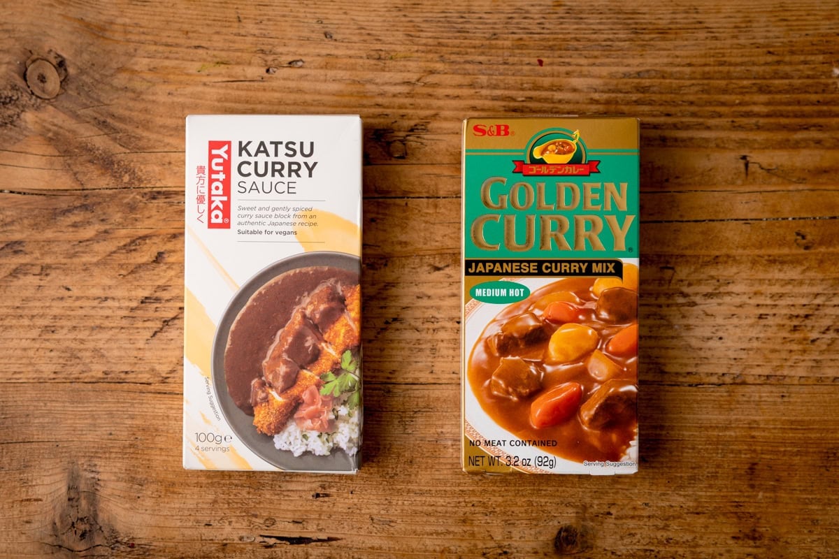 Two boxes of Japanese curry blocks on a wooden surface: Yutaka Katsu Curry Sauce (left) and S&B Golden Curry Mix (right).
