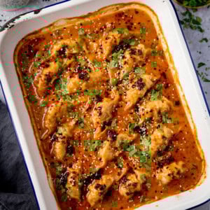 Baked dumplings in a rectangular dish, topped with a spicy orange curry sauce, sesame seeds, and chopped coriander.