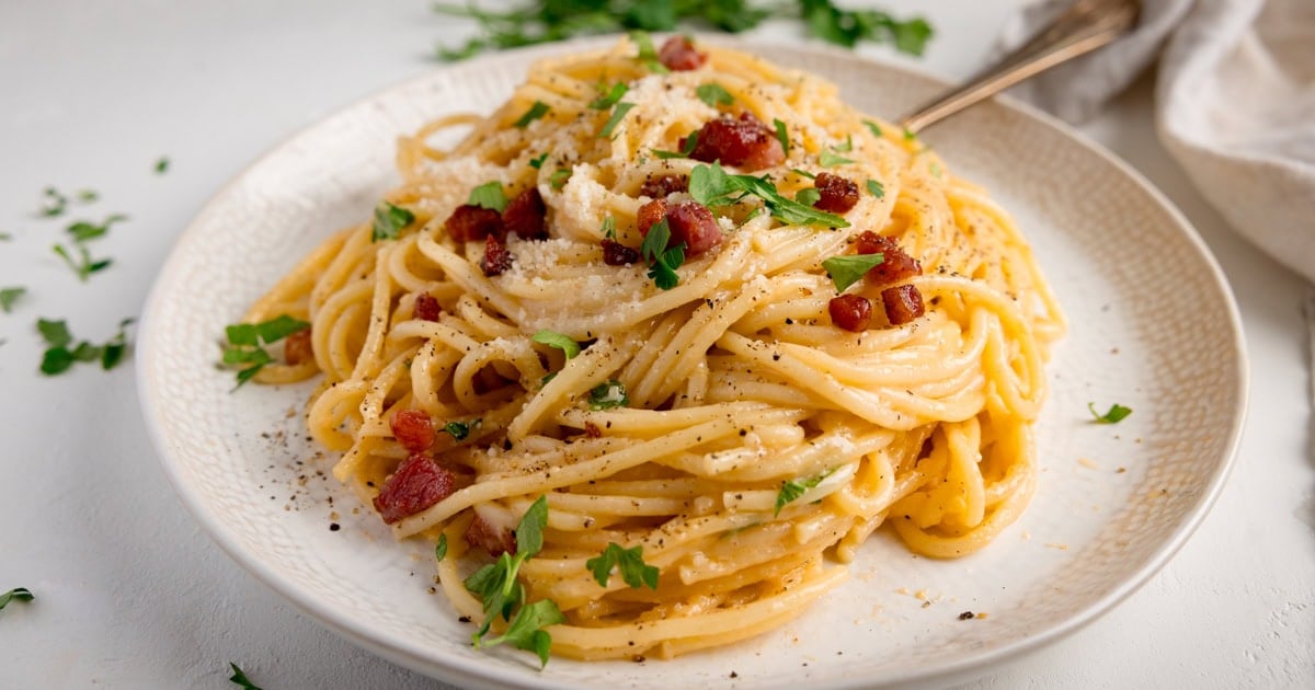 Spaghetti with crispy diced pancetta and grated parmesan sprinkled with parsley on a white plate 