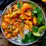 A bowl of white rice topped with Thai Chicken Curry, red peppers, chopped chilli, fresh coriander and lime wedges, with a fork on the side—a delicious take on classic Thai Red Curry.
