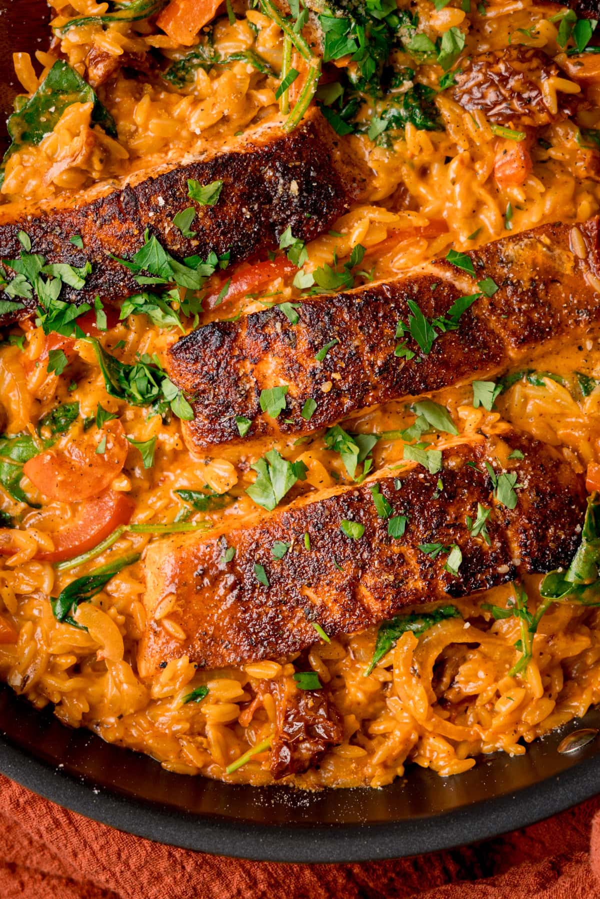 Close up overhead image of a dark pan filled with Tuscan-style orzo and pan fried salmon fillets on top, garnished with parsley.