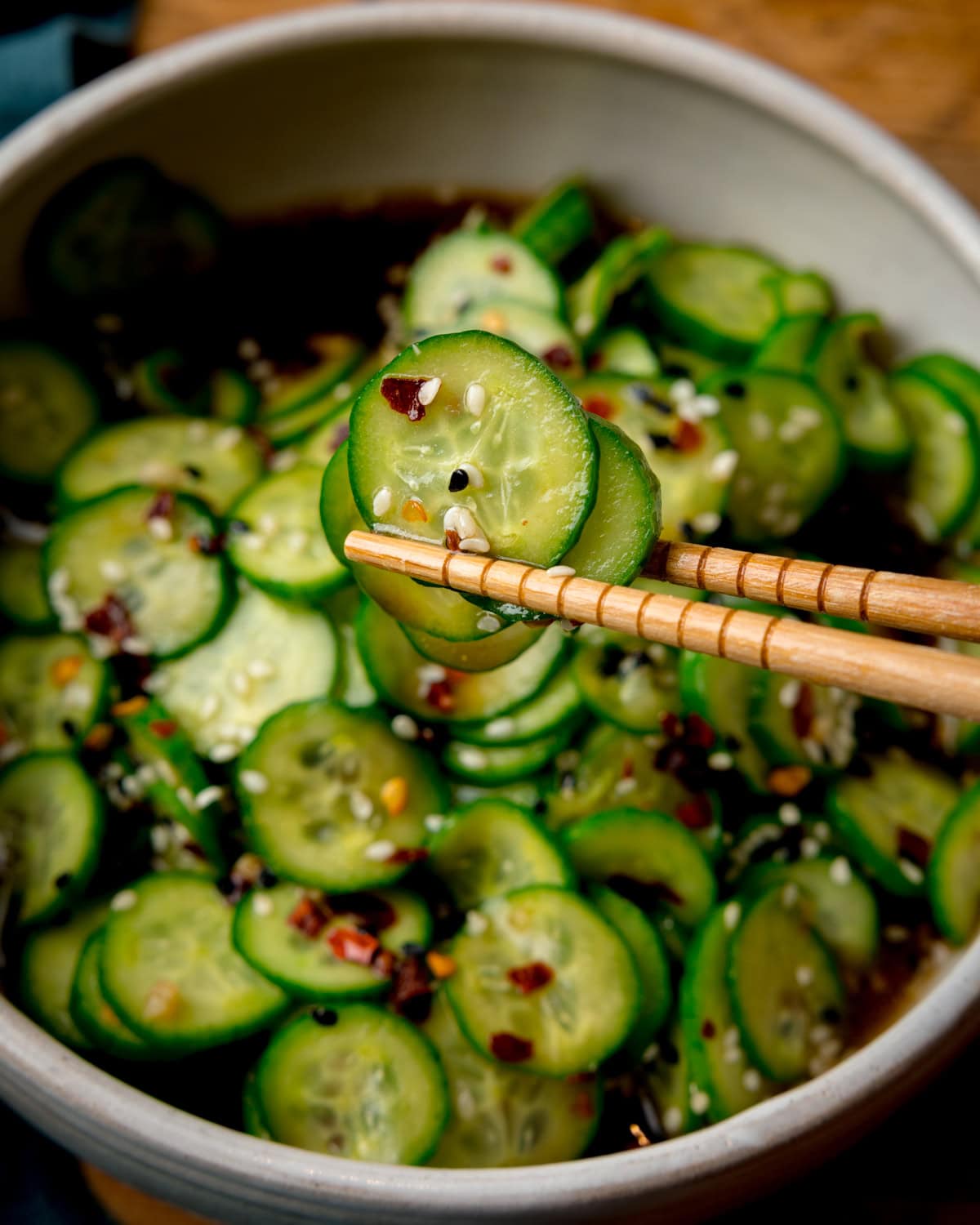 Chopsticks hold a slice of cucumber above a bowl of Asian Cucumber Salad.