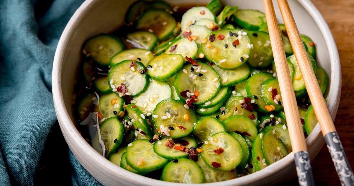 A white bowl with sliced cucumber in a dark liquid dressing, sprinkles with chilli flakes 