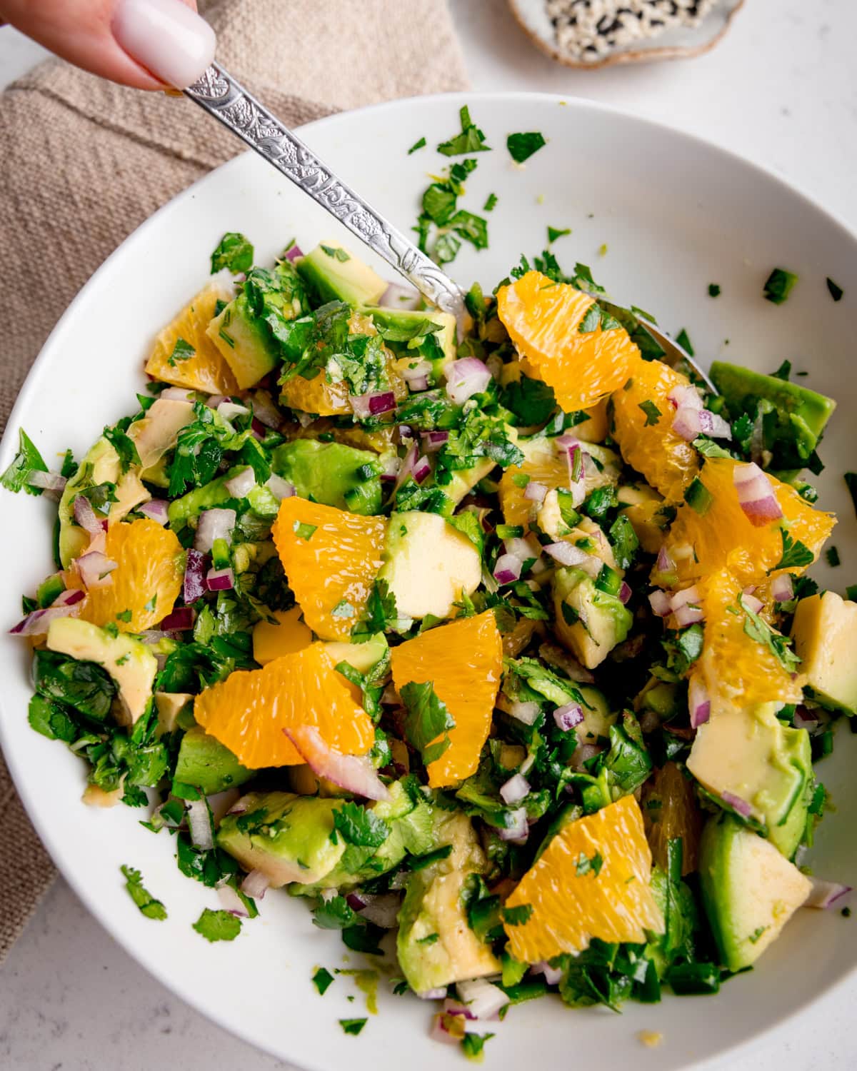 A white bowl with avocado orange salsa, with a spoon taking some of the salsa.