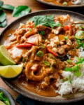 A side-on image of a plate of Thai Panang beef Curry with tender beef, peppers, jasmine rice, lime wedges, chopped peanuts, and spring onions, garnished with Thai basil and spring onions.
