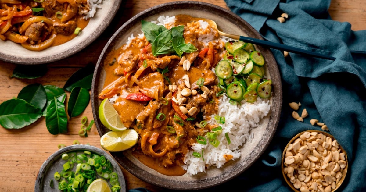 Strips of beef in a creamy red Thai curry sauce with white rice, pickled cucumber and peanuts
