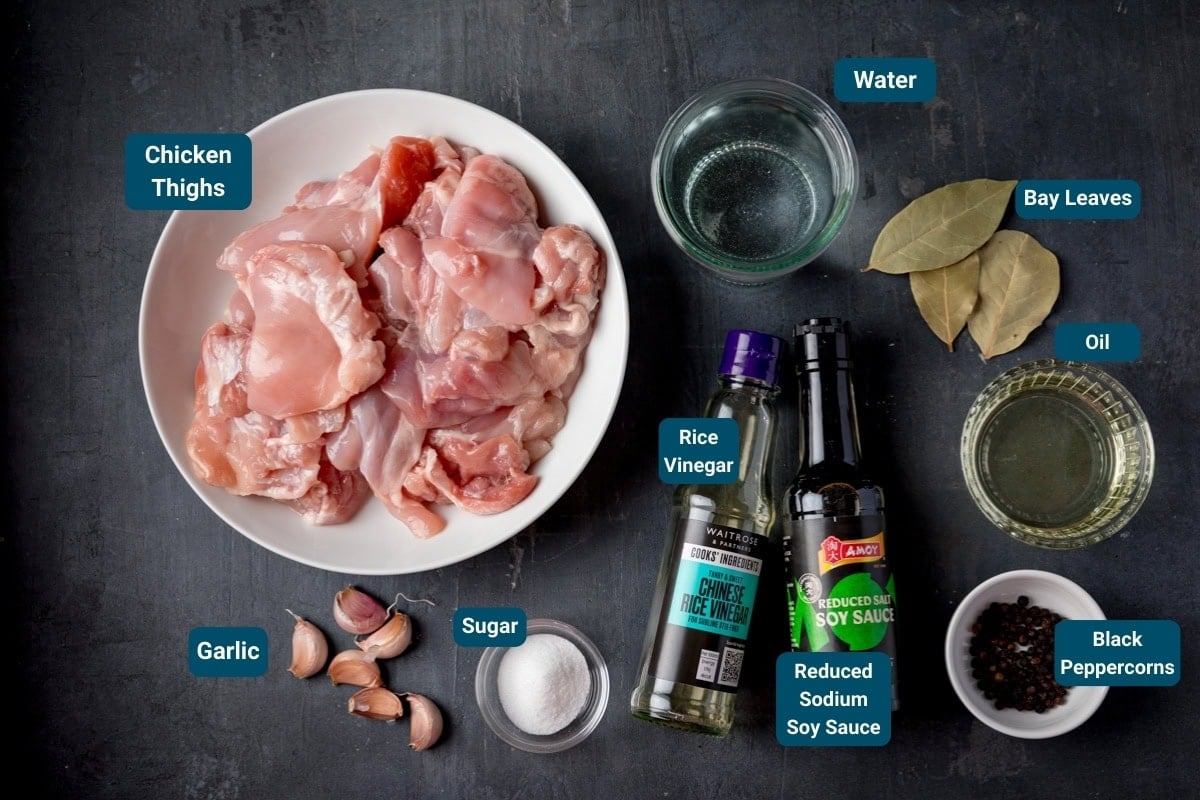 Ingredients for Chicken Adobo on a dark background - Including: garlic, sugar, rice vinegar, reduced salt soy sauce, water, bay leaves, oil, and black peppercorns.