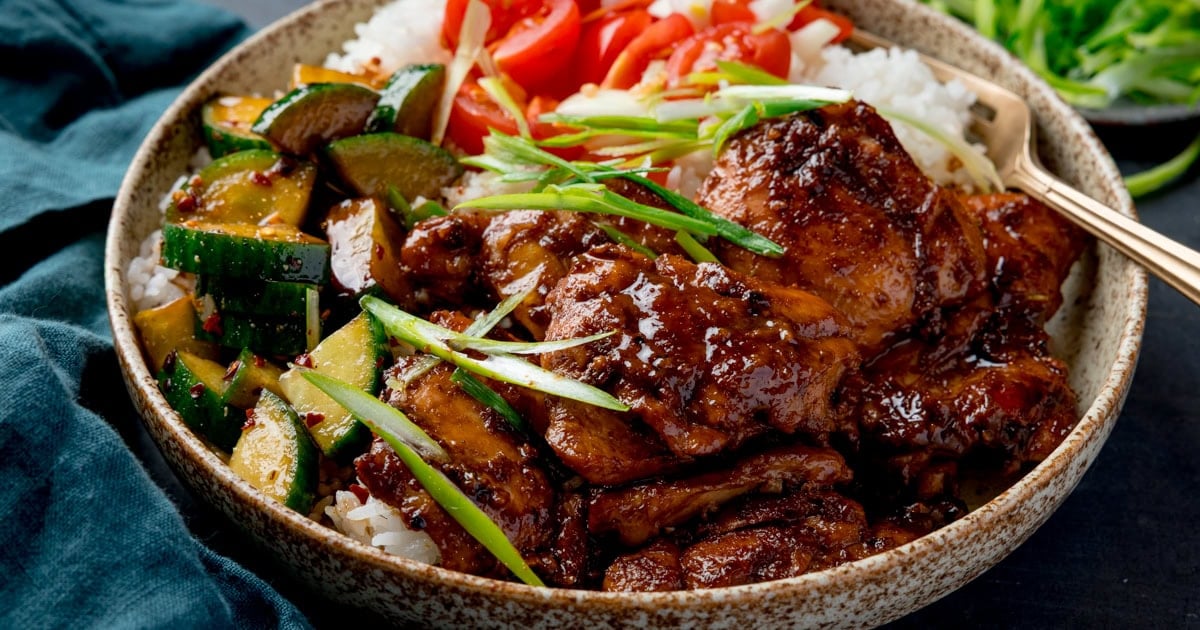 Glazed chicken thighs in a bowl with white rice diced tomatoes and pickled cucumber