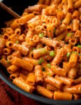A close-up of rigatoni pasta coated in a creamy Gochujang pasta sauce, topped with grated cheese, black pepper, and chopped spring onions.