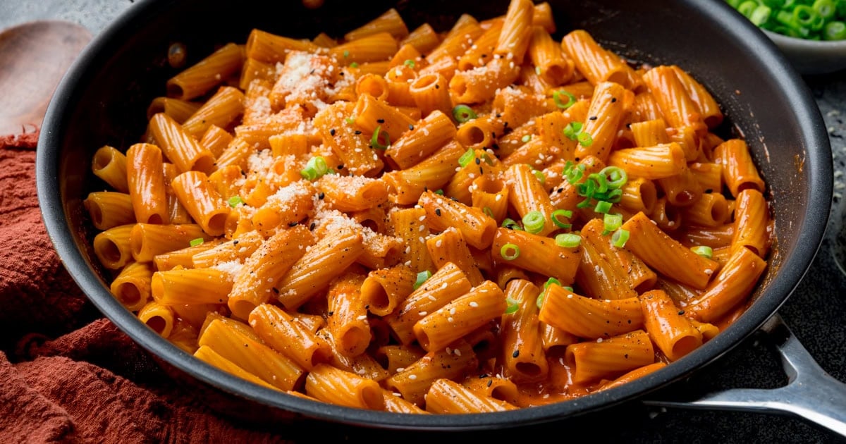 A black bowl full of rigatoni pasta coated in a creamy tomato sauce sprinkled with chopped scallions