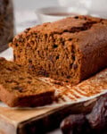 A loaf of sliced raisin and date malt loaf sits on baking parchment, with a single slice cut and placed in front.
