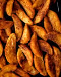 Close-up of crispy potato wedges, baked or fried to a golden brown and arranged in a single layer, highlighting their tempting texture.