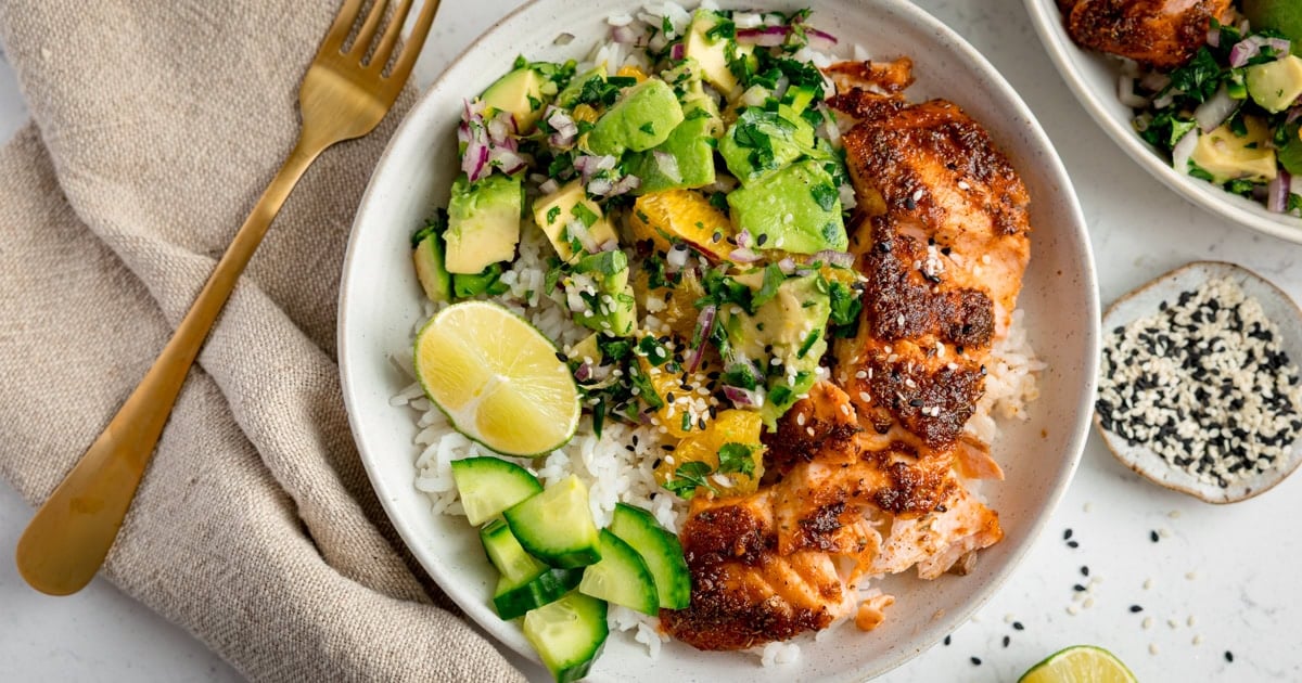 A bowl of white rice topped with cajun salmon fillet and diced avocado and orange salsa.