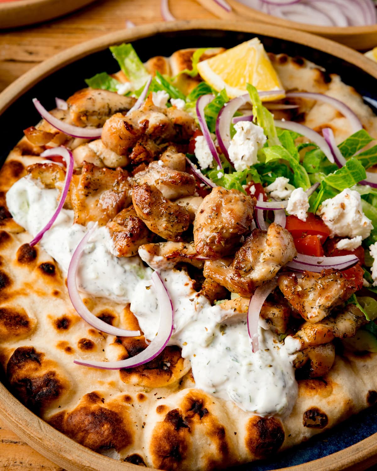 Chicken Souvlaki with tzatziki, lettuce, tomato, red onion and feta on toasted flatbread with a lemon wedge.