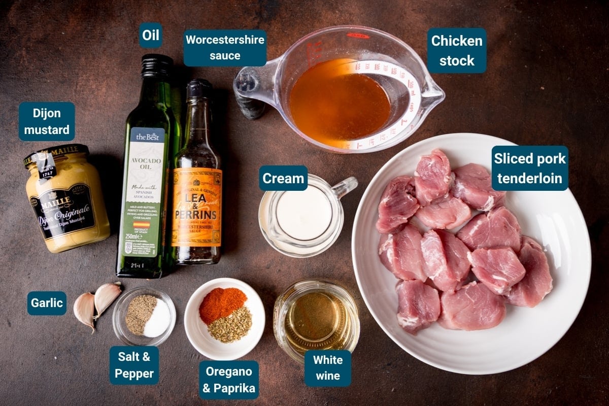 Ingredients for a Pork Tenderloin recipe, including sliced pork, mustard, oil, garlic, cream, stock, wine, Worcestershire sauce, spices&mdash;ideal for a rich and creamy Dijon sauce&mdash;are arranged on a dark surface with labels.