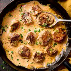 Pan of seared pork fillet medallions in a creamy Dijon sauce, garnished with chopped parsley, with a spoon lifting one piece.