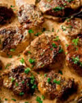 Close up of seared pork fillet medallions in a creamy Dijon sauce, garnished with chopped fresh parsley.