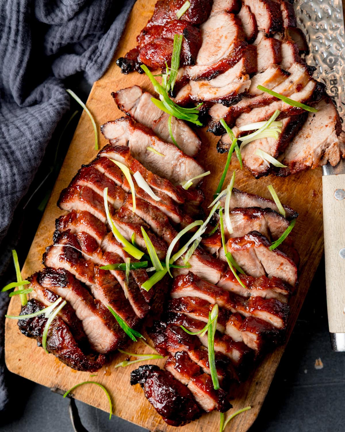 Sliced Chinese BBQ pork arranged on a wooden chopping board, garnished with thin strips of spring onion.