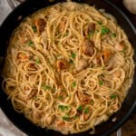 Overhead square image of a skillet filled with creamy Garlic Butter Chicken Pasta, pan-fried chicken pieces, chopped parsley, and a sprinkle of black pepper on top.
