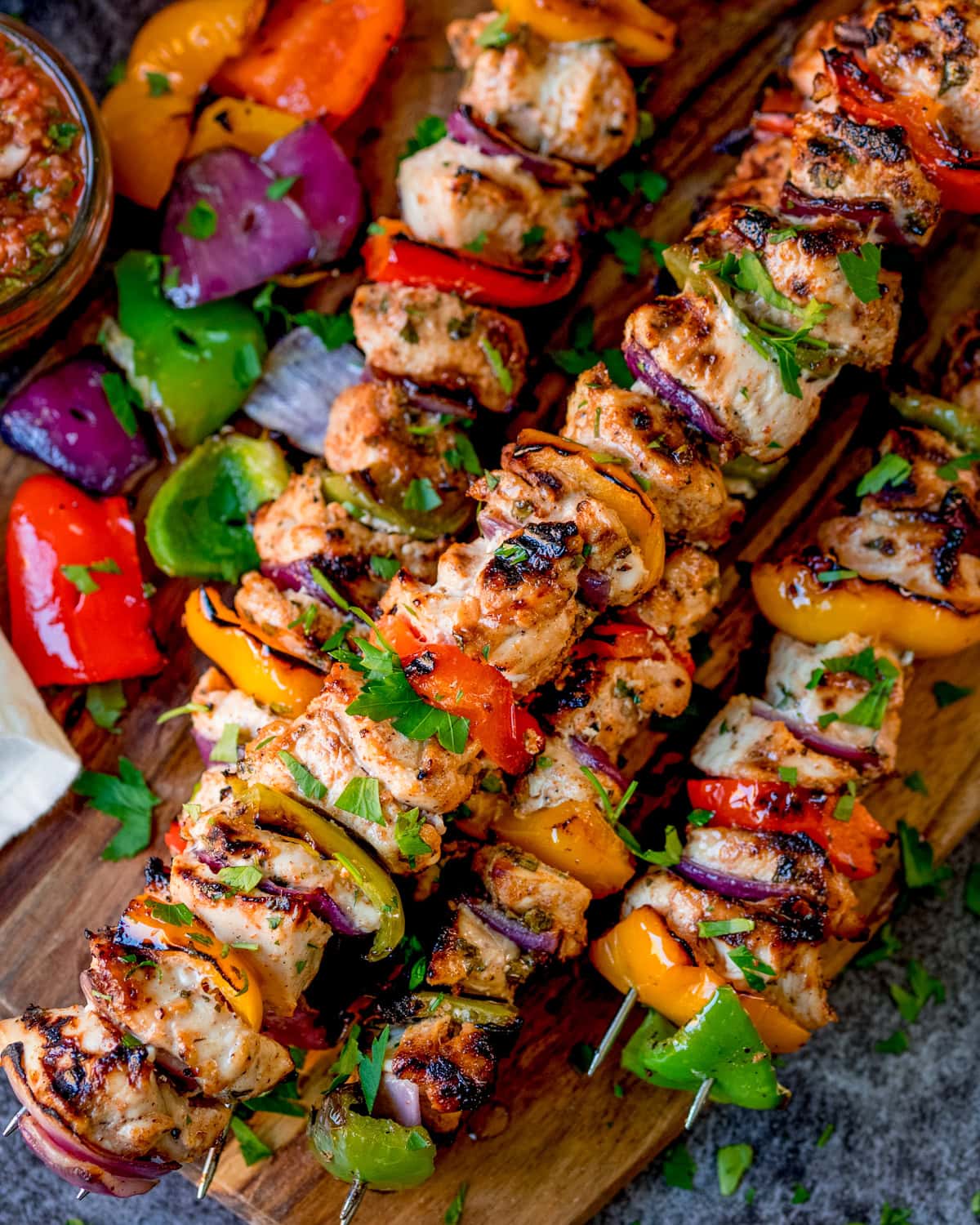 Grilled chicken and vegetable kebabs with peppers and onions, garnished with herbs, served on a wooden board.