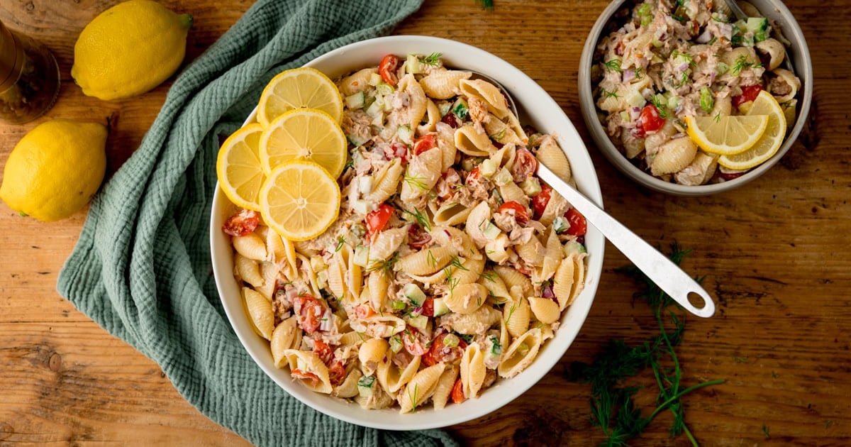 A bowl of pasta shells, diced cucumber, chopped tomatoes, flaked tuna in a creamy dressing.