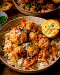 A bowl of rice topped with Tuscan chicken meatballs in a creamy tomato sauce, garnished with herbs and grated cheese, served with a slice of garlic bread on the side. A further bowl, some garlic bread and a little pot of parsley is also in shot.