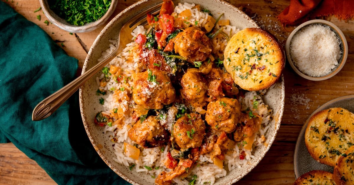 A bowl of white rice topped with 6 chicken meatballs in a creamy tomato sauce.