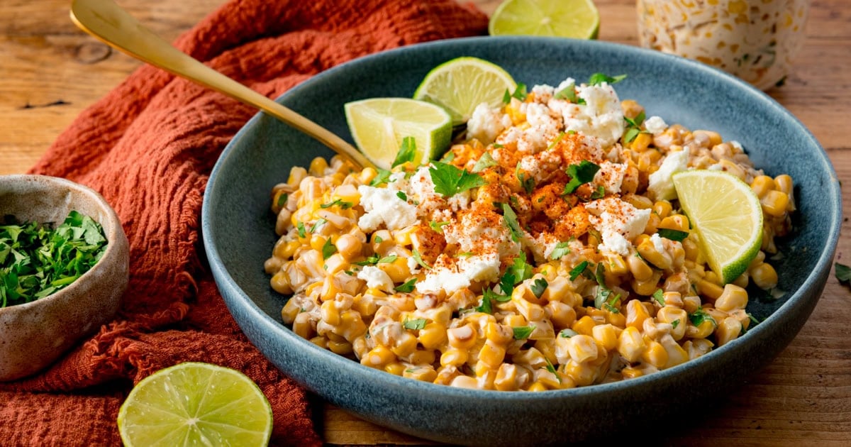 A grey bowl with creamed corn sprinkled with white cheese and chopped coriander.