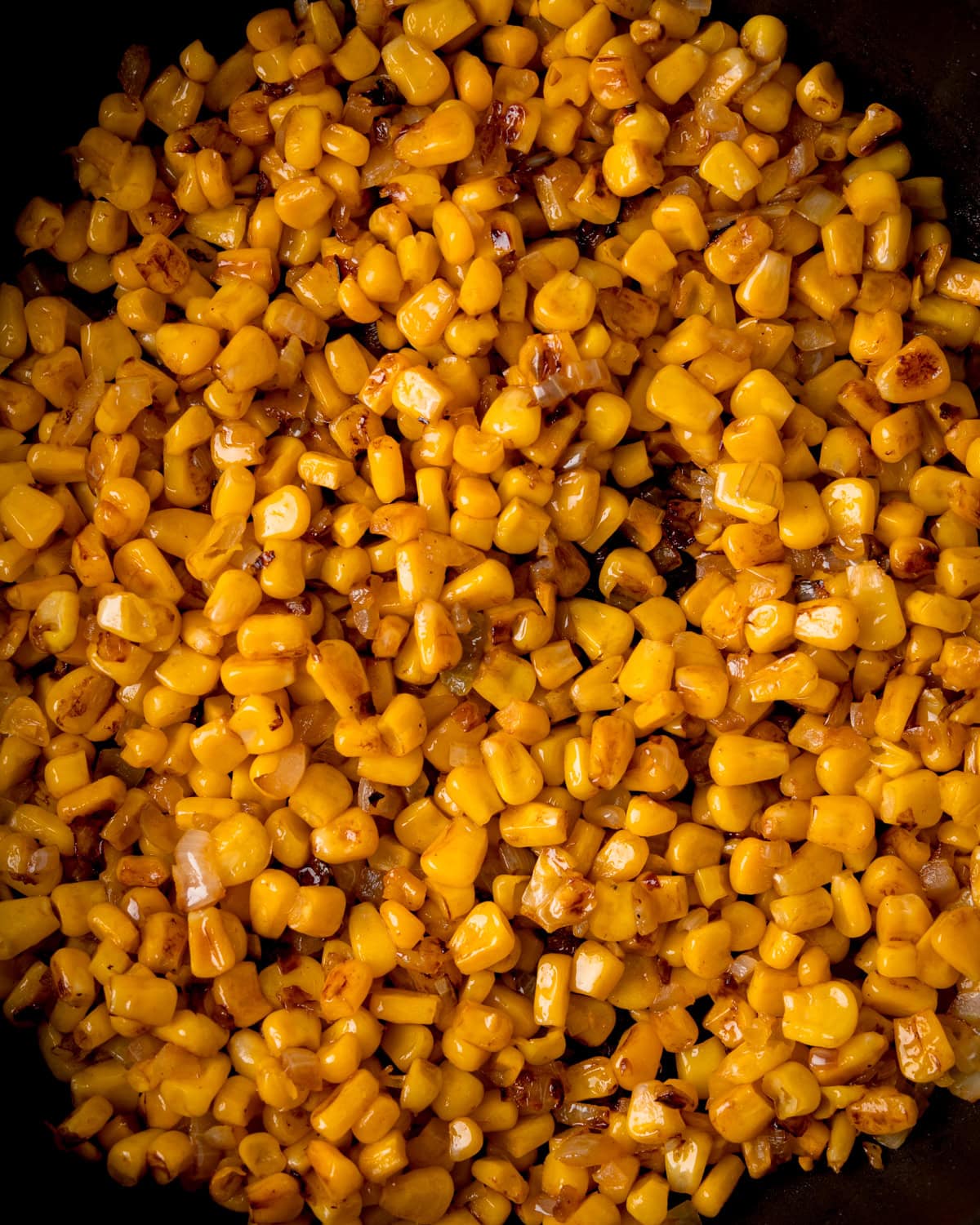 Close-up of cooked sweetcorn kernels with a slight char, glistening with oil in a pan.