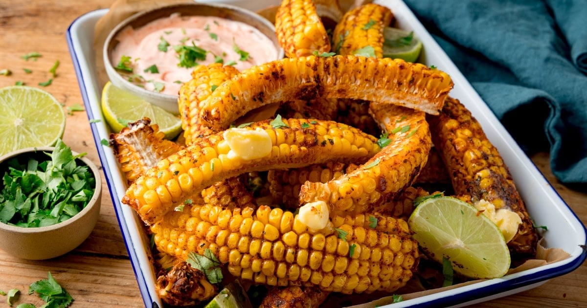 A rectangle tin dish with charred, curled strips of sweetcorn with a small dish of spicy mayo