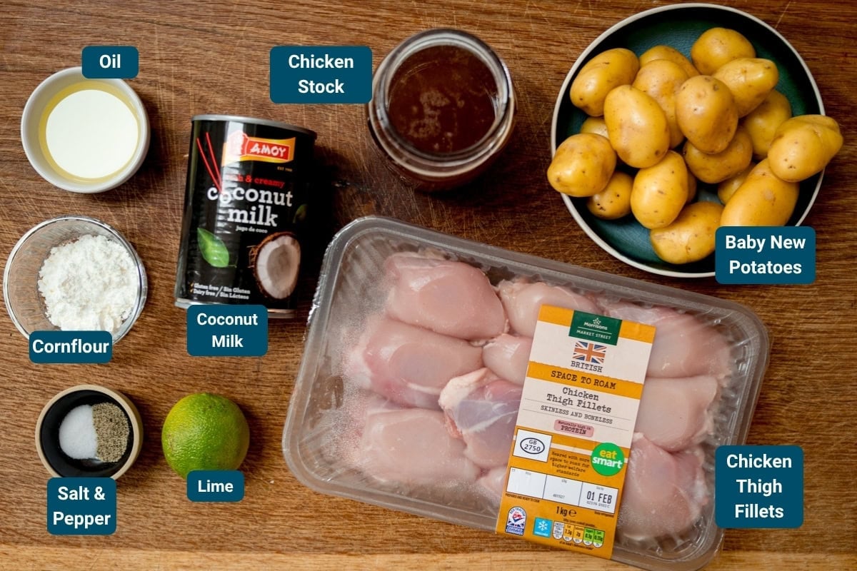Ingredients for Massaman Chicken Curry laid out on a wooden surface, including chicken thigh fillets, baby potatoes, coconut milk, chicken stock, oil, cornflour, lime, salt and pepper. Ingredients are labelled.