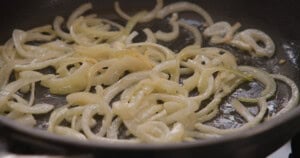 Sliced onions being sautéed in a frying pan with oil.