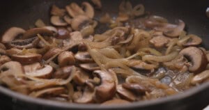 Sliced mushrooms and onions cooking in a frying pan with some liquid.