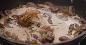 Sliced mushrooms and onions simmer in a creamy sauce with a dollop of soured cream and Worcestershire sauce in a frying pan.