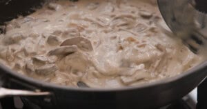 Creamy mushroom stroganoff sauce cooking in a frying pan, with sliced mushrooms visible in the thick, pale-coloured mixture.