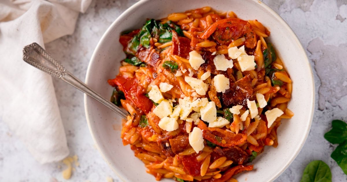 A white bowl with orzo in a bacon and tomato sauce topped either crumbled cheese.