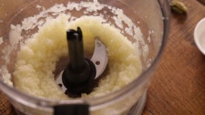 Finely chopped onions and garlic inside a food processor bowl on a wooden worktop.