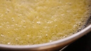 Close-up of finly minced onions and garlic bubbling in a frying pan on a hob.