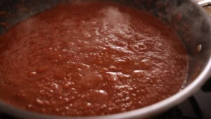 A close-up view of tomato sauce simmering and bubbling in a pan on a hob.