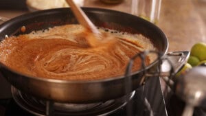 A person stirs a curry sauce in a frying pan on a hob.
