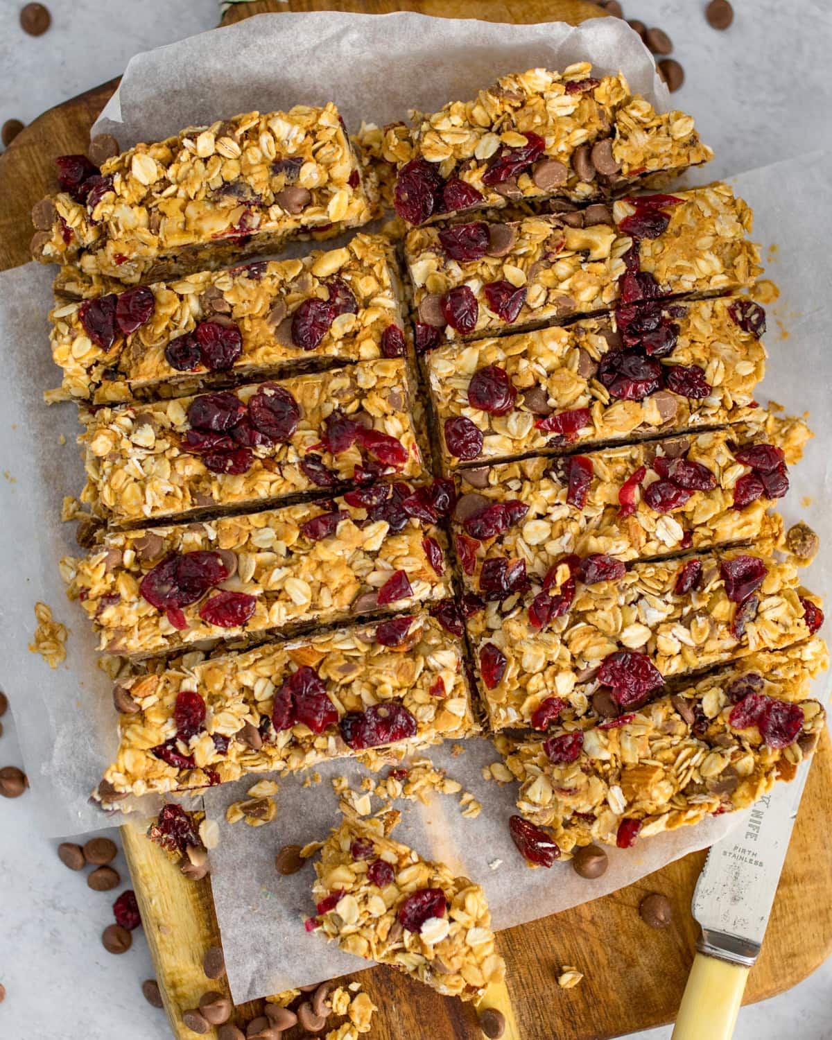 Overhead image of sliced peanut butter cranberry granola bars on baking parchment, with a knife beside them.