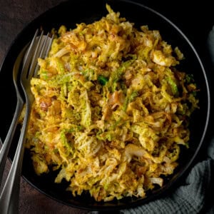 Overhead image of a black bowl filled with sauteed cabbage with a fork and spoon on the side.